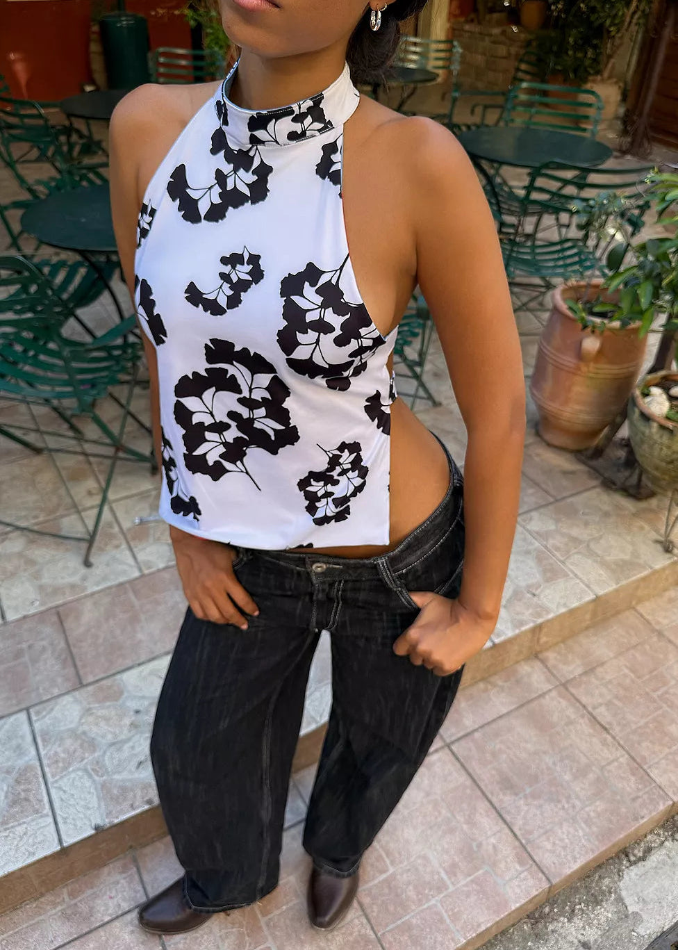 Person wearing a white top with black floral patterns and black pants in an outdoor setting.
