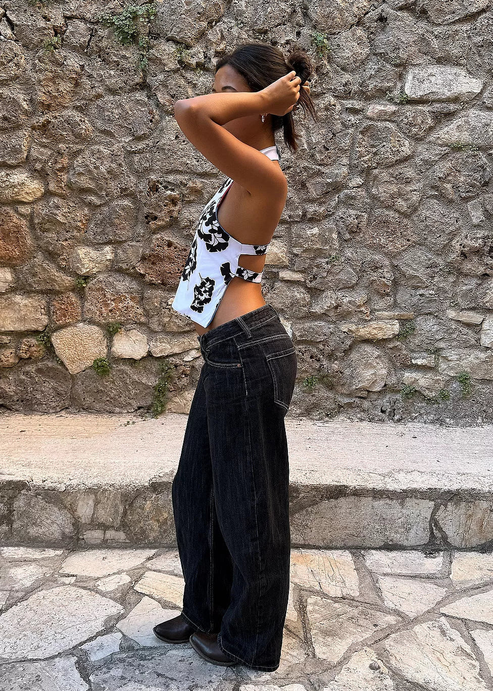 Person wearing a patterned top and black pants against a stone wall.
