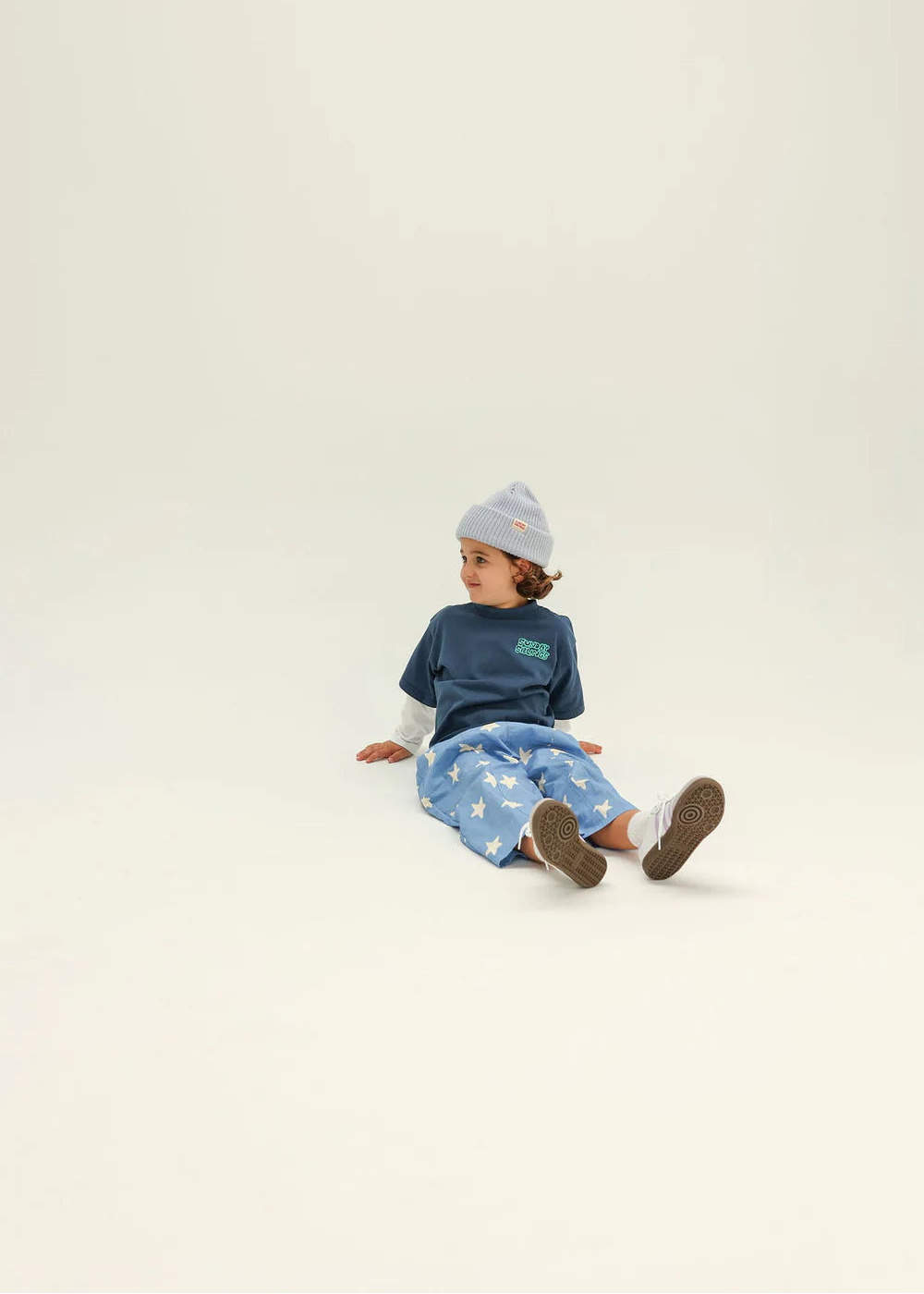 Child wearing a blue outfit with a logo, sitting on a white background
