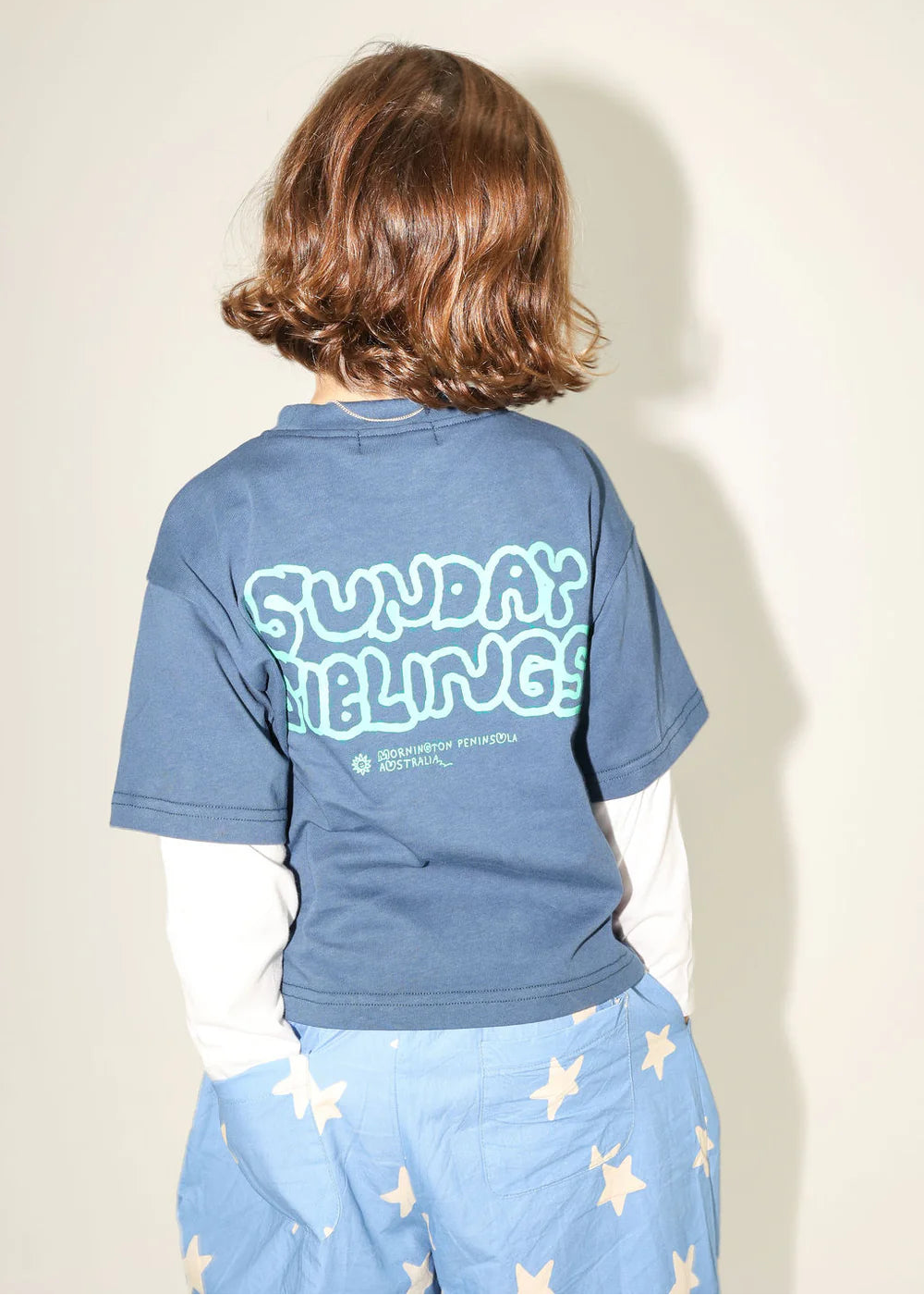 Person wearing a blue t-shirt with text on the back, standing against a plain background
