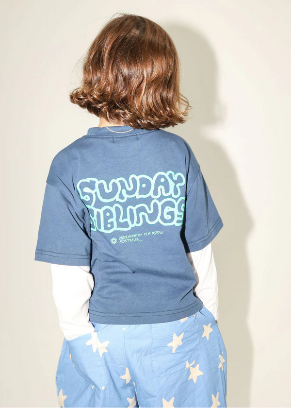 Person wearing a blue t-shirt with text on the back, standing against a plain background