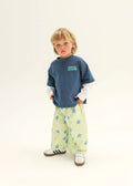 Child wearing a blue shirt with text and light green pants with star patterns on a white background
