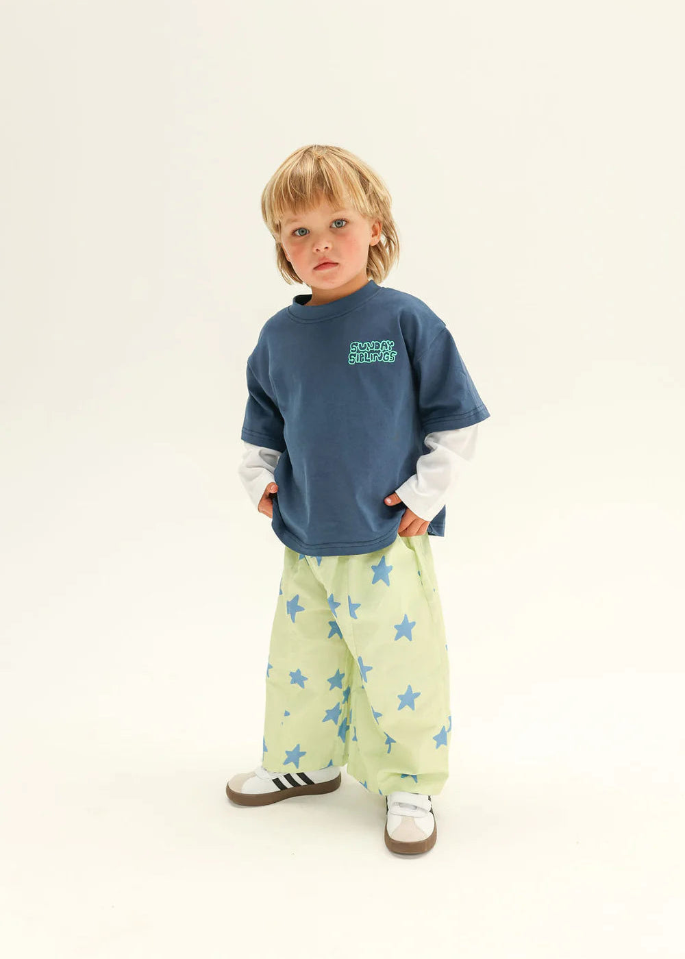 Child wearing a blue shirt with text and light green pants with star patterns on a white background