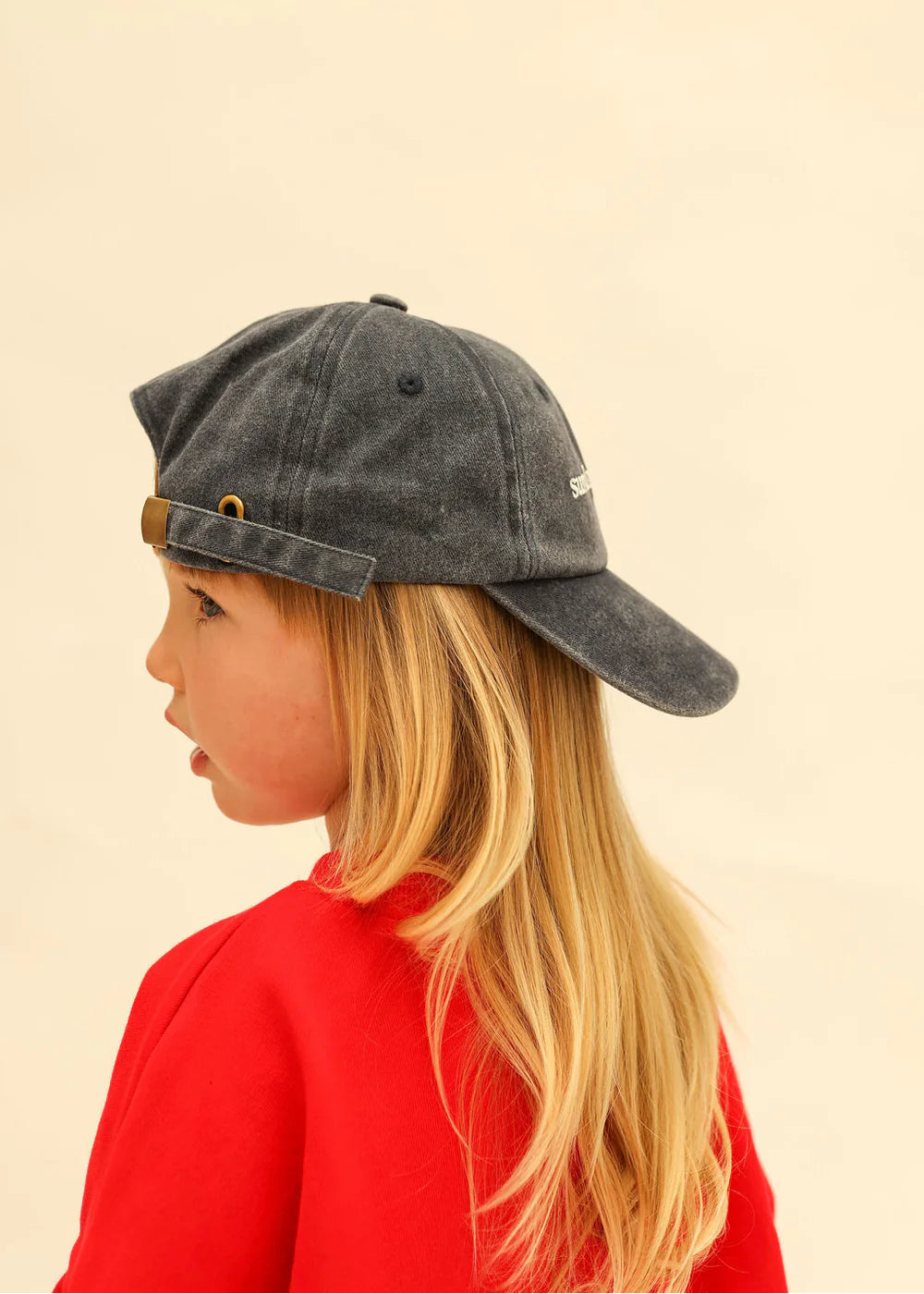 Child wearing a denim cap and red jacket on a beige background
