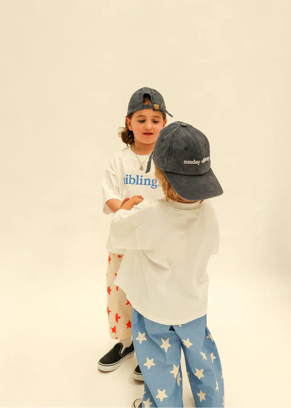 Two children wearing matching baseball caps and sweatshirts against a plain background