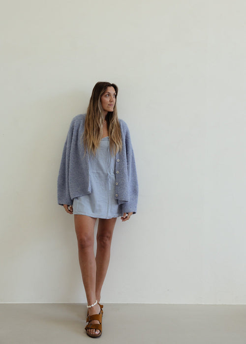 Woman wearing a blue cardigan and dress against a plain background