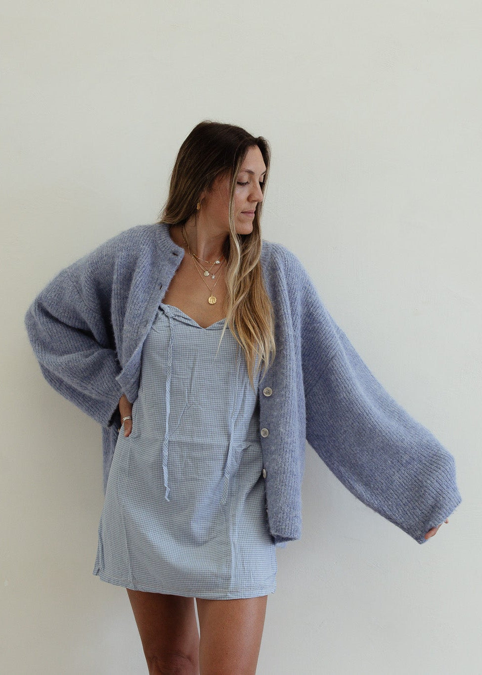 Woman wearing a light blue cardigan over a denim dress against a plain background