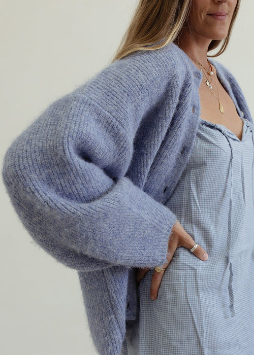 Woman wearing a light blue cardigan over a matching dress against a plain background