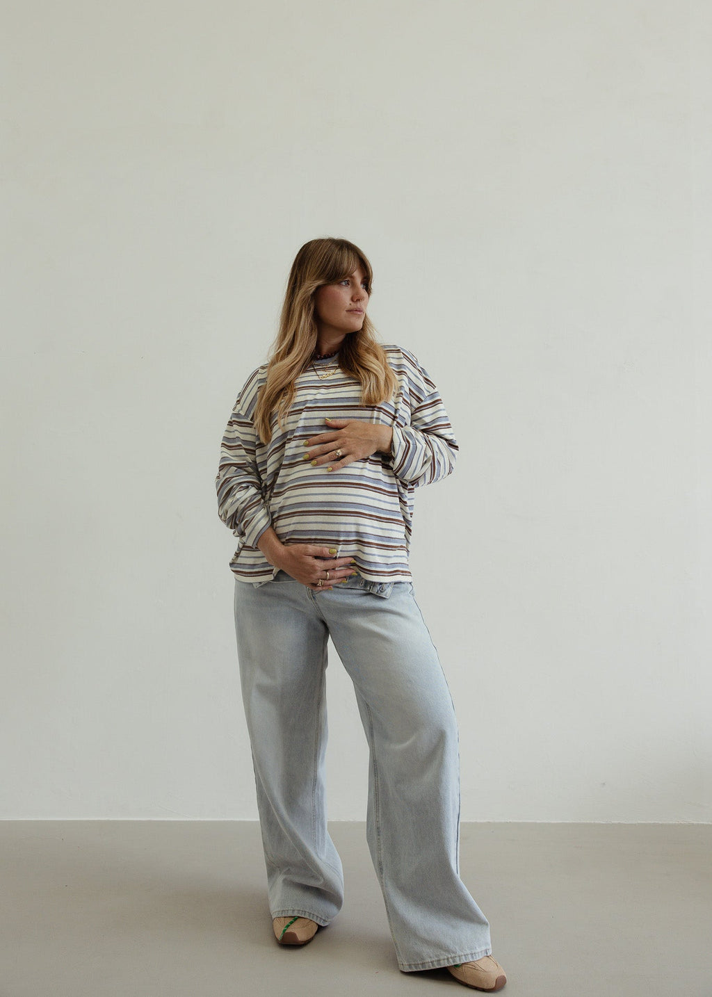Pregnant woman wearing a striped shirt and jeans against a plain background
