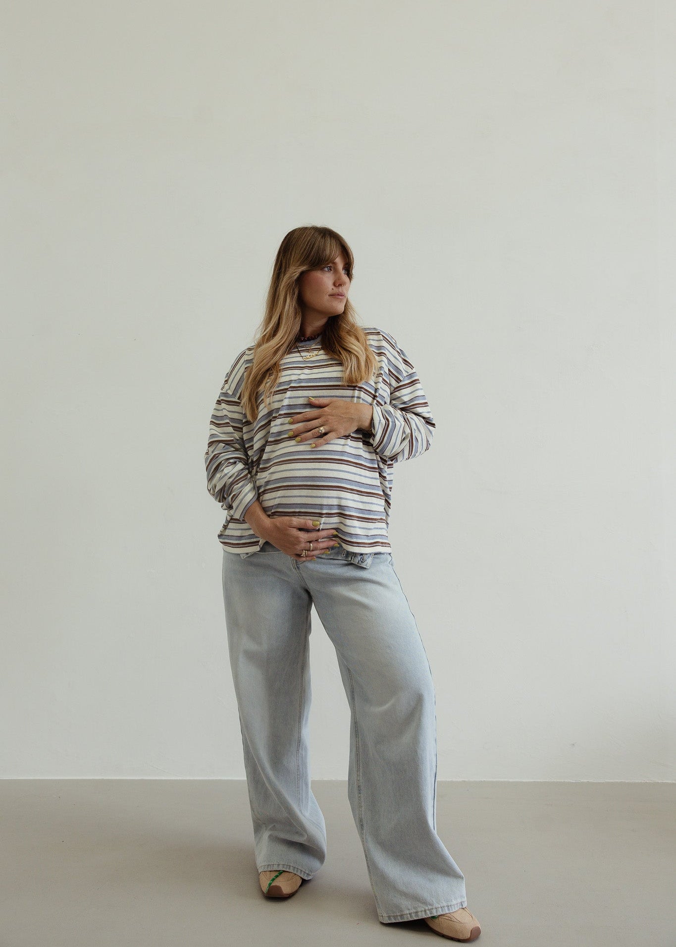Pregnant woman wearing a striped shirt and jeans against a plain background