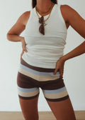 Woman wearing a white sleeveless top and striped shorts against a plain background