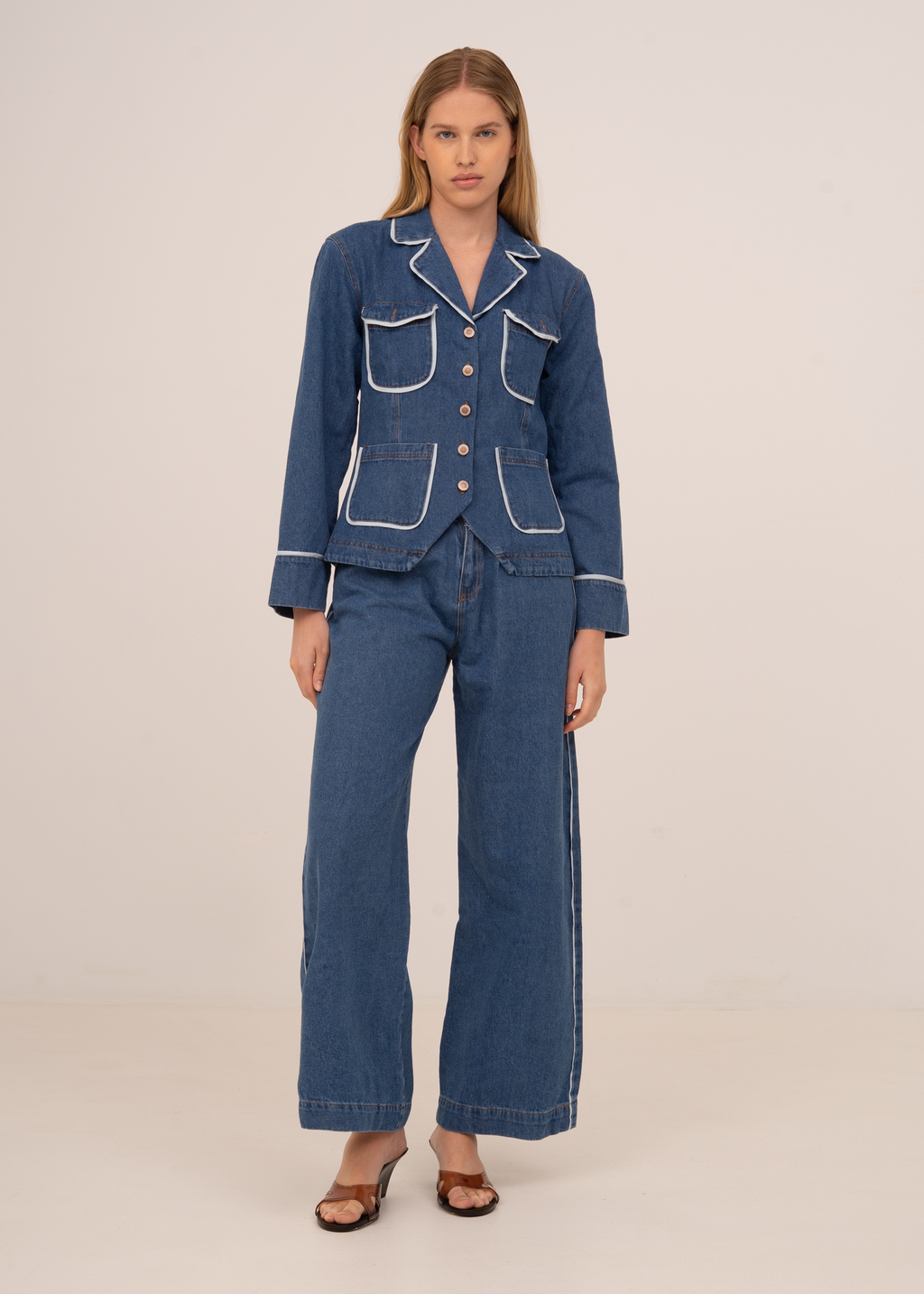 Woman wearing a blue denim suit with white piping on a beige background