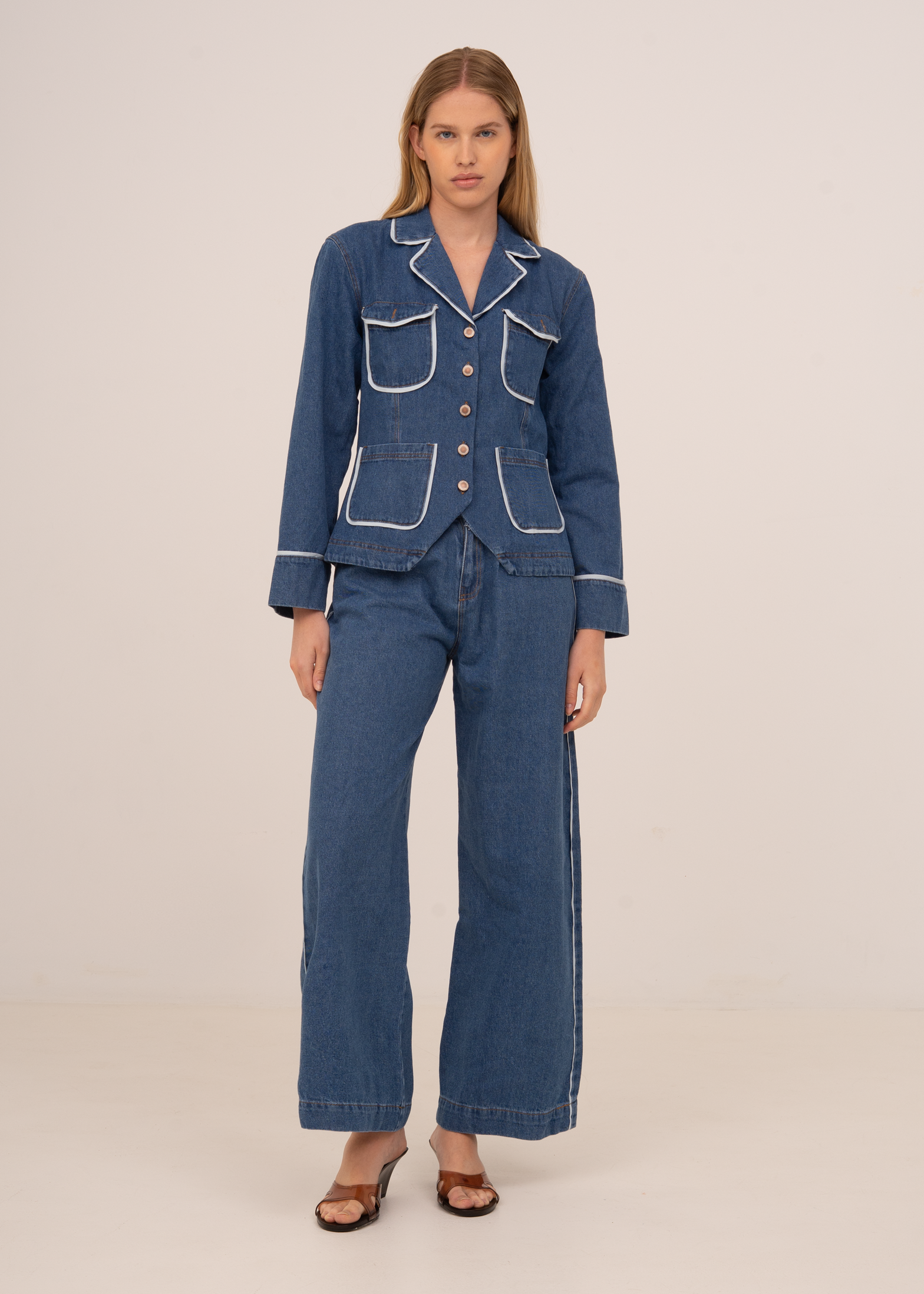 Woman wearing a blue denim suit with white piping on a beige background