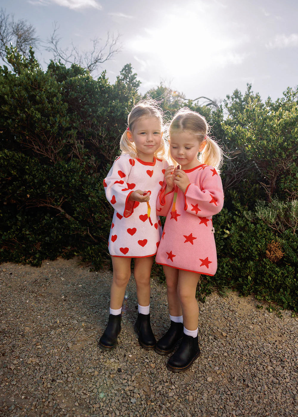 Two young girls in colorful dresses standing outdoors with greenery in the background