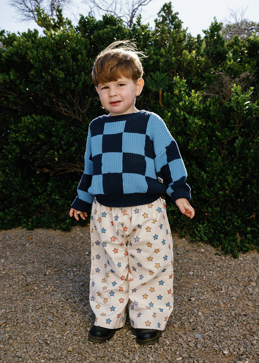 Child wearing a blue checkered sweater and star-patterned pants standing outdoors.