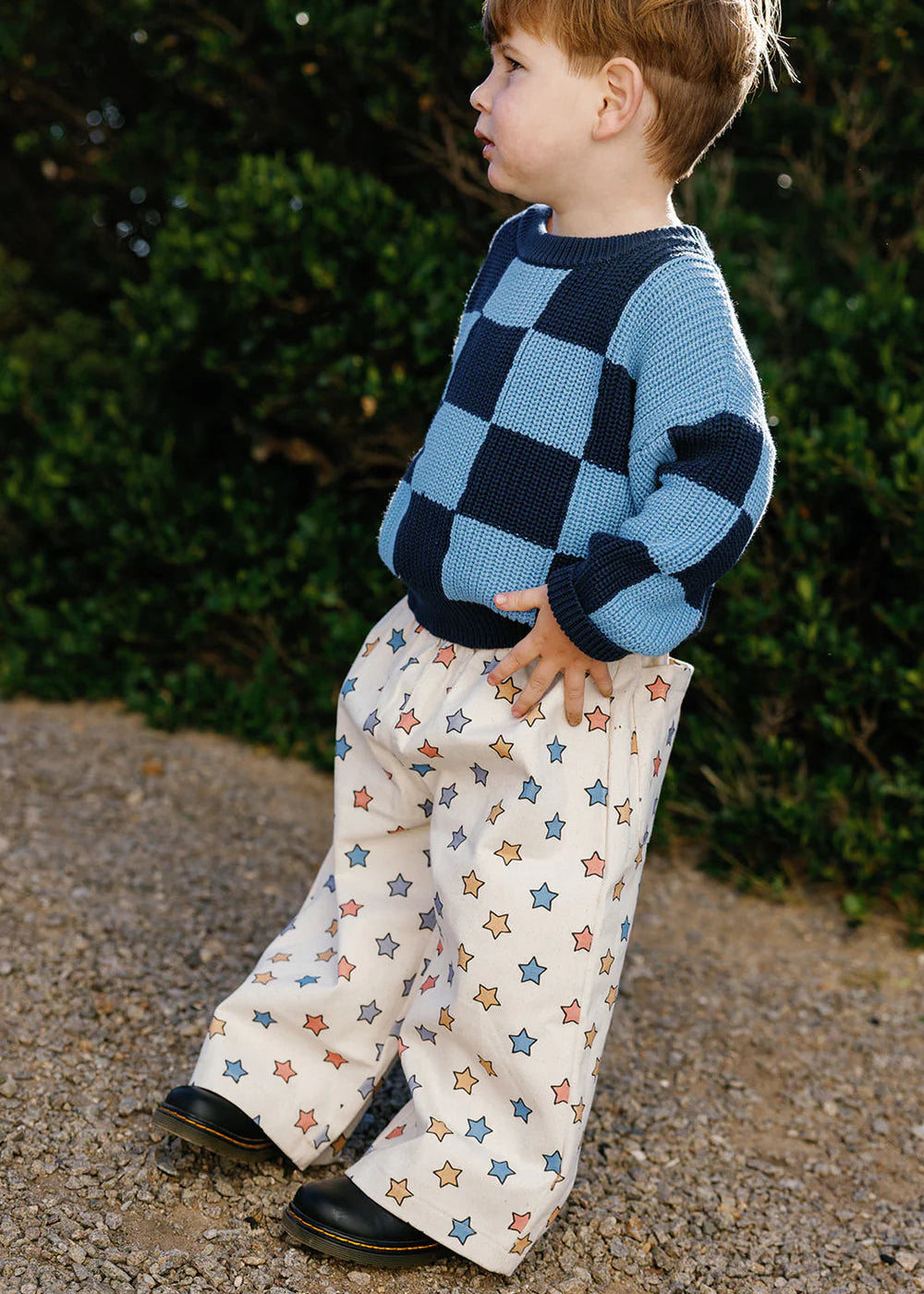 Child wearing a blue checkered sweater and star-patterned pants standing outdoors.