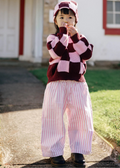 Child wearing a striped sweater and pants standing on a sidewalk.