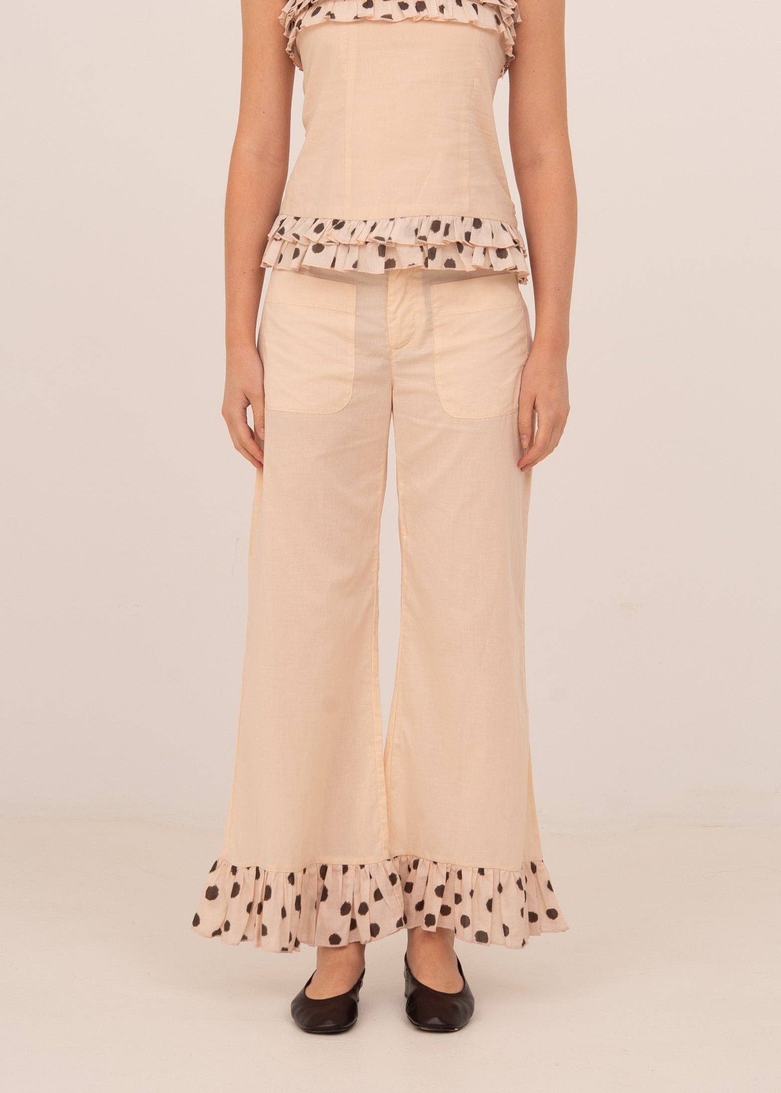 Woman wearing a beige top and wide-leg pants with ruffled hem on a light background
