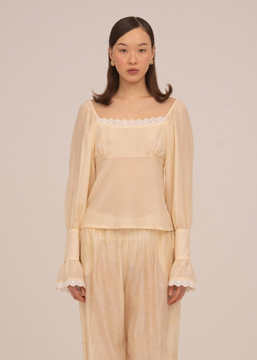 Woman wearing a beige blouse and pants against a plain background