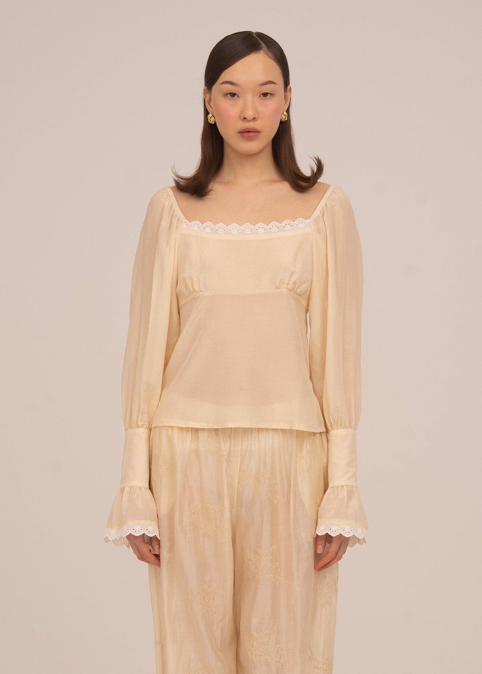 Woman wearing a beige blouse and pants against a plain background