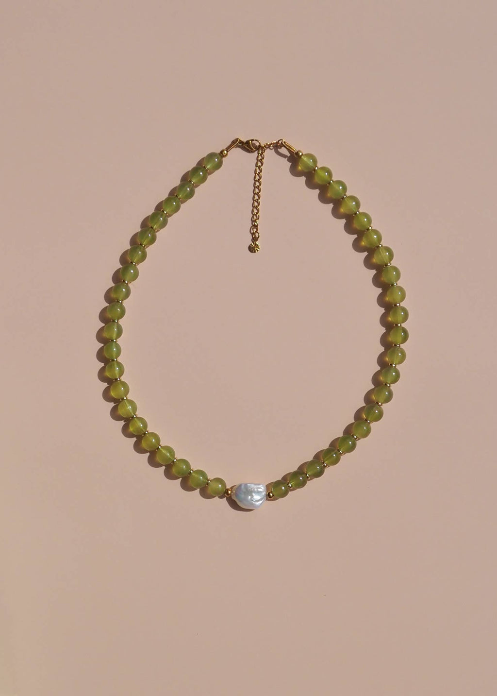 Necklace with green beads and a silver pendant on a beige background
