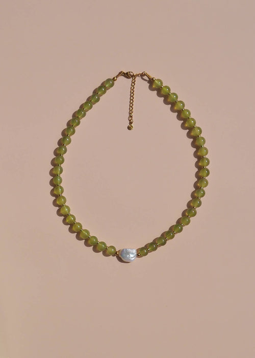 Necklace with green beads and a silver pendant on a beige background