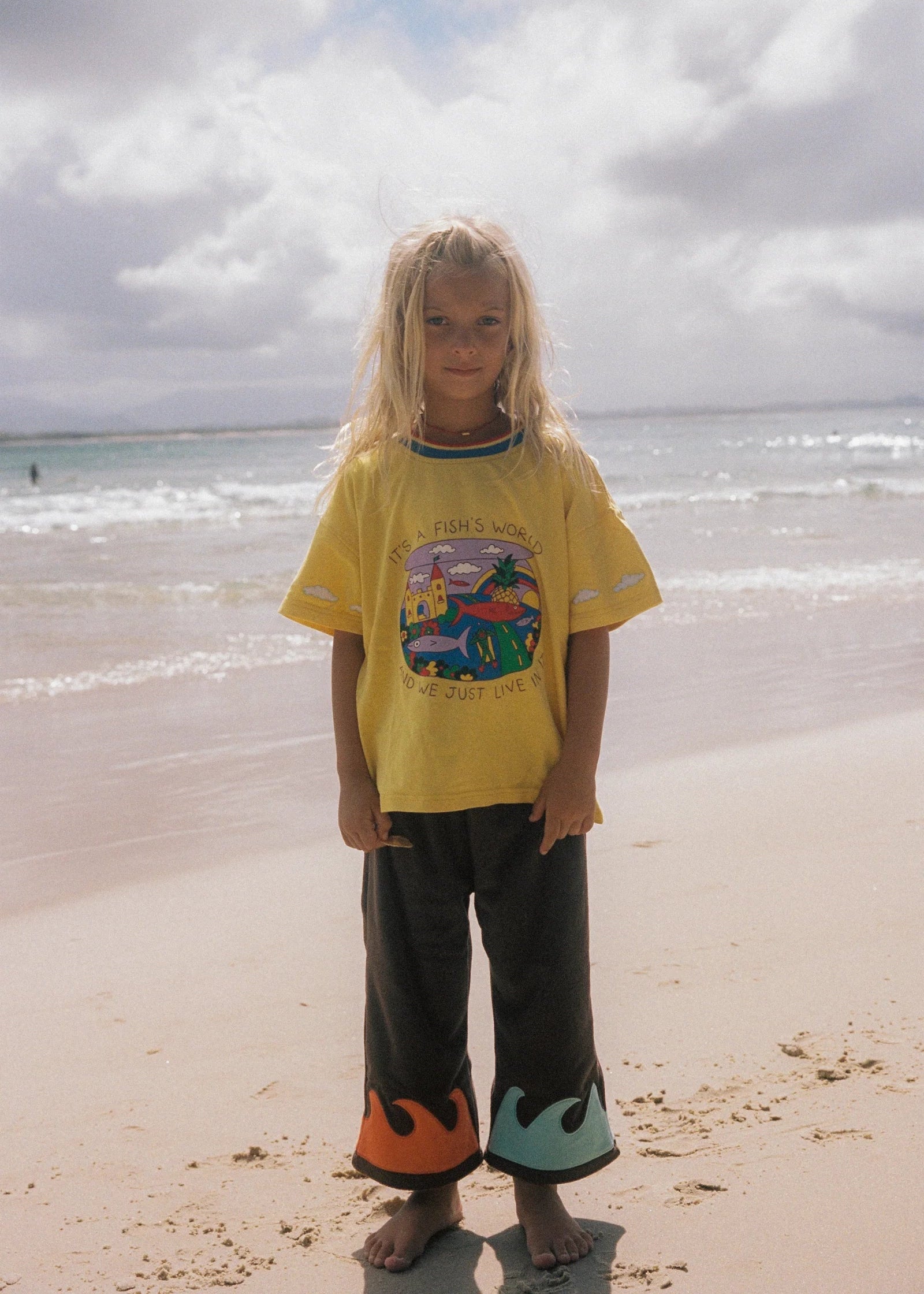 Child wearing a yellow shirt with a graphic design on a beach