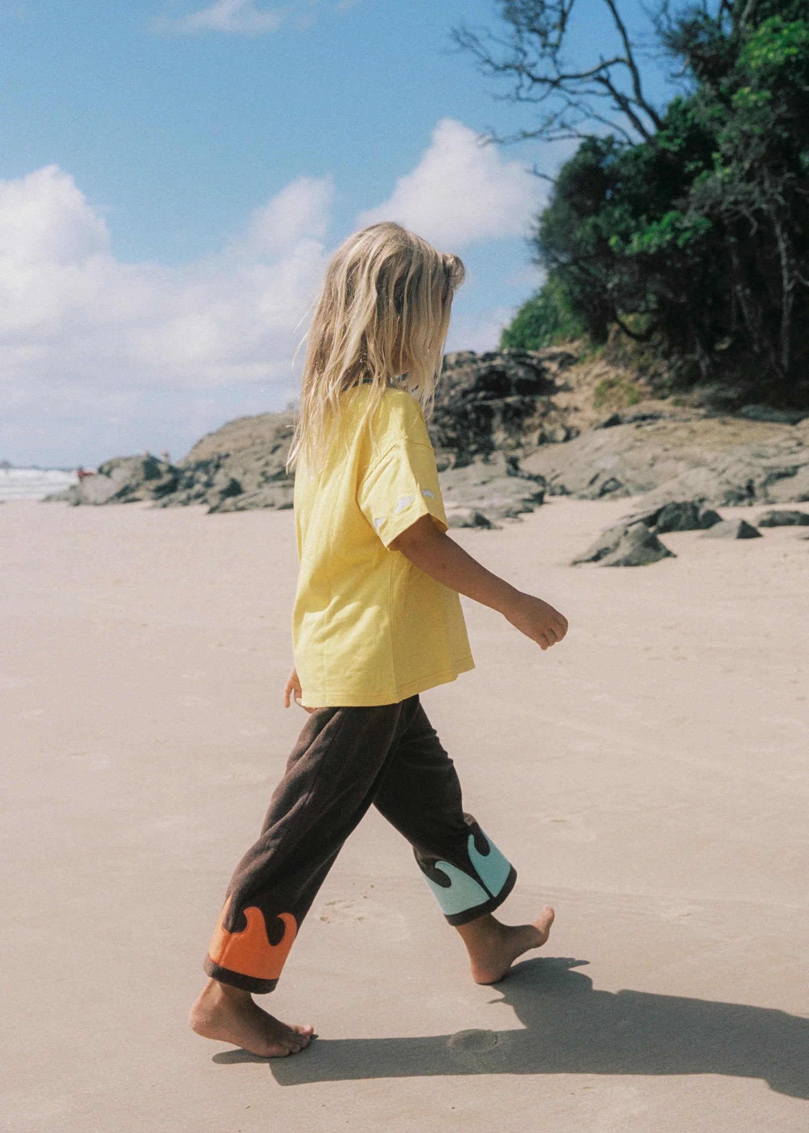 Person walking on a sandy beach with a clear sky and greenery in the background