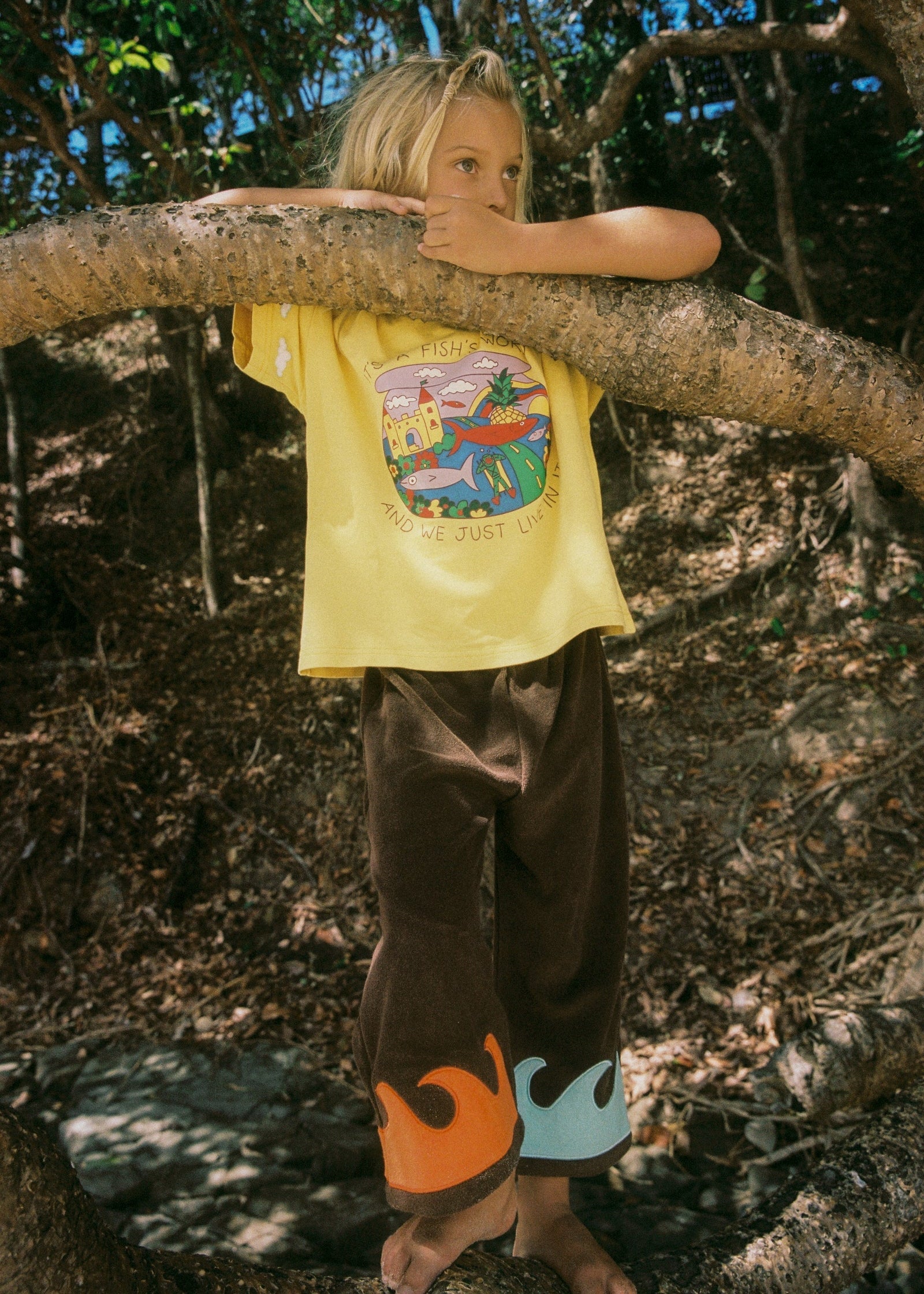 Child in a yellow shirt with a colorful design, standing in a forest.