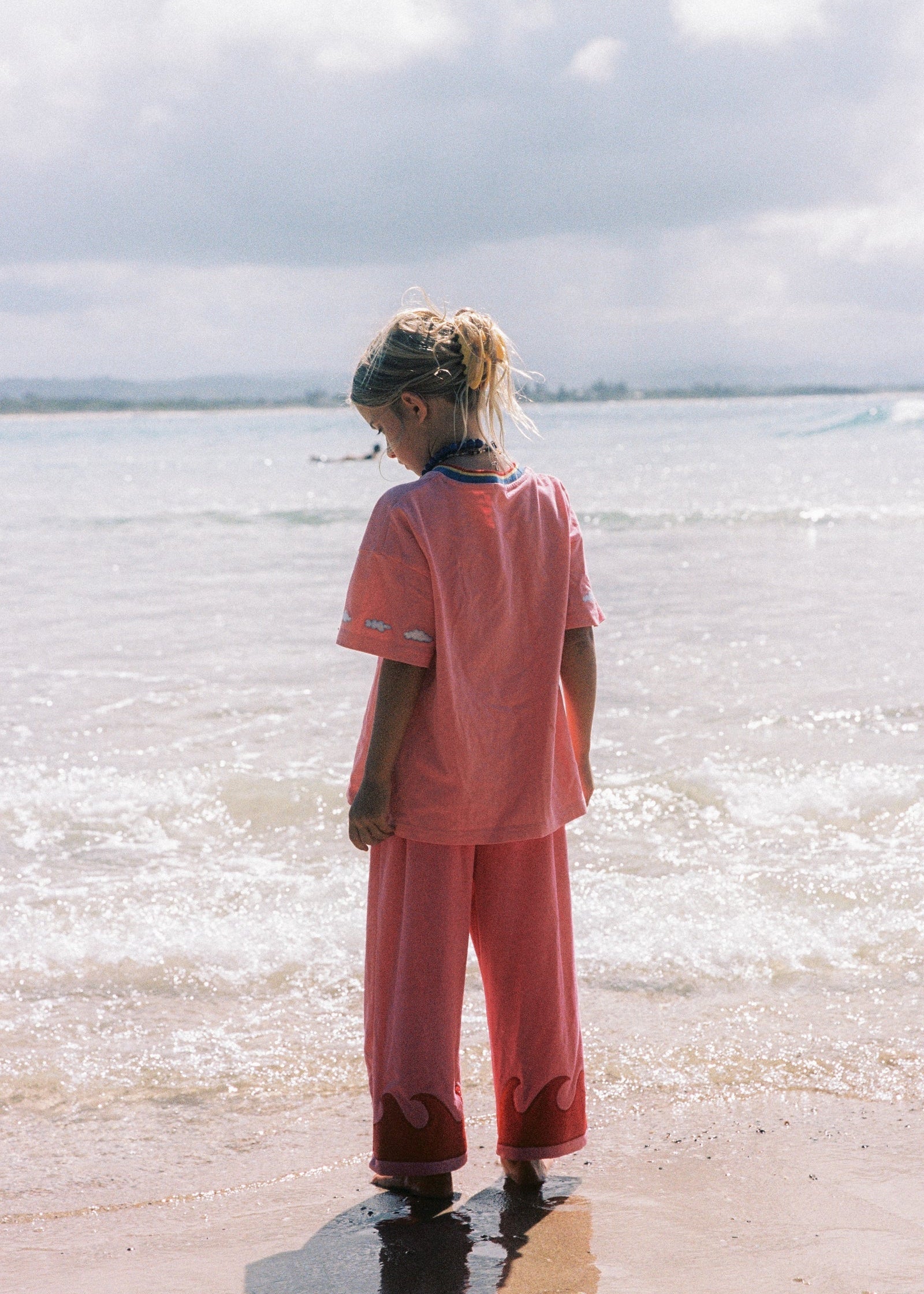 Person in a pink outfit standing on a beach with waves and sky in the background
