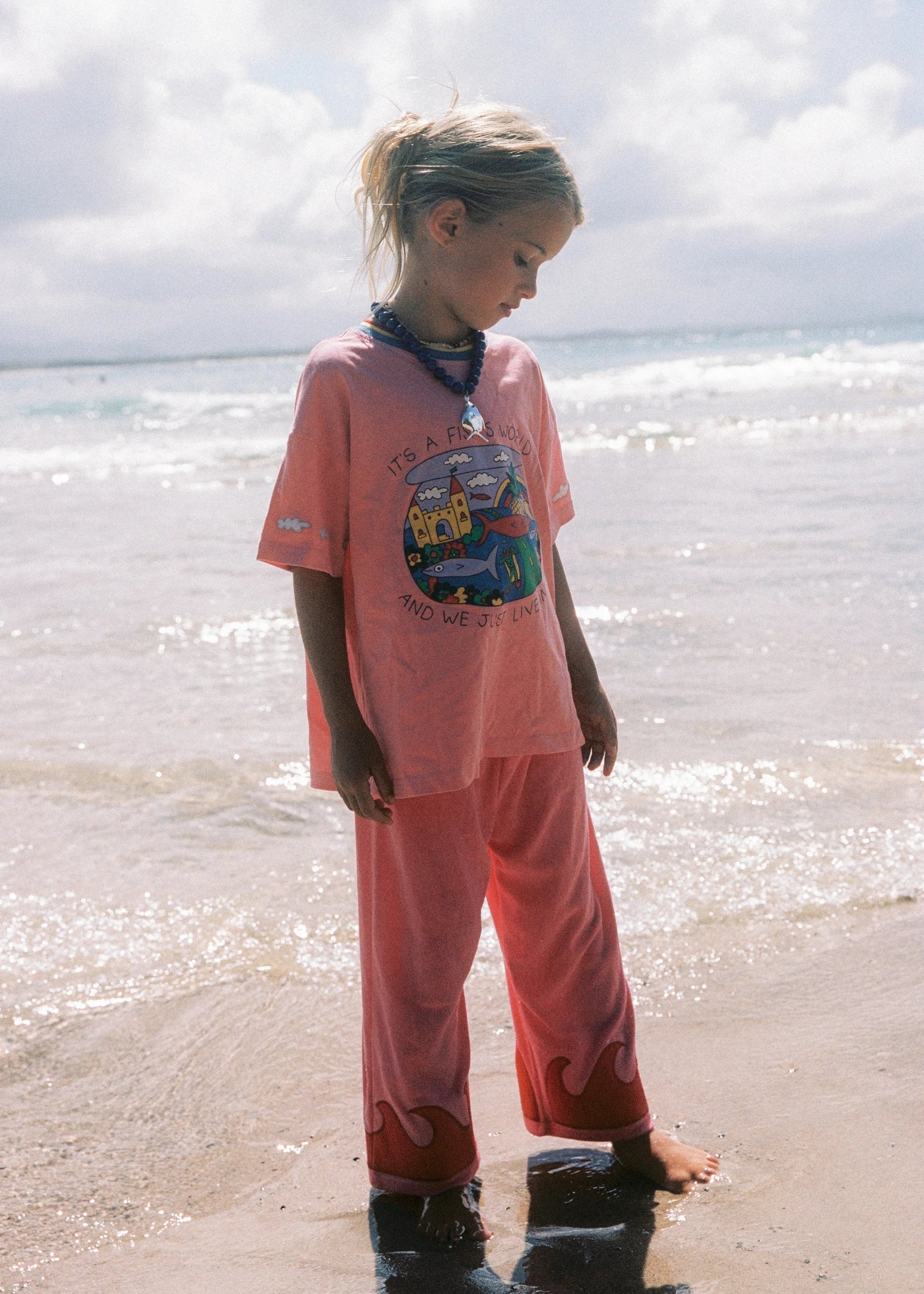 Child in pink outfit standing on a beach with ocean waves in the background