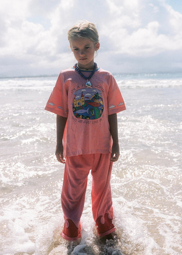 Child in a pink outfit standing in shallow water with a cloudy sky.