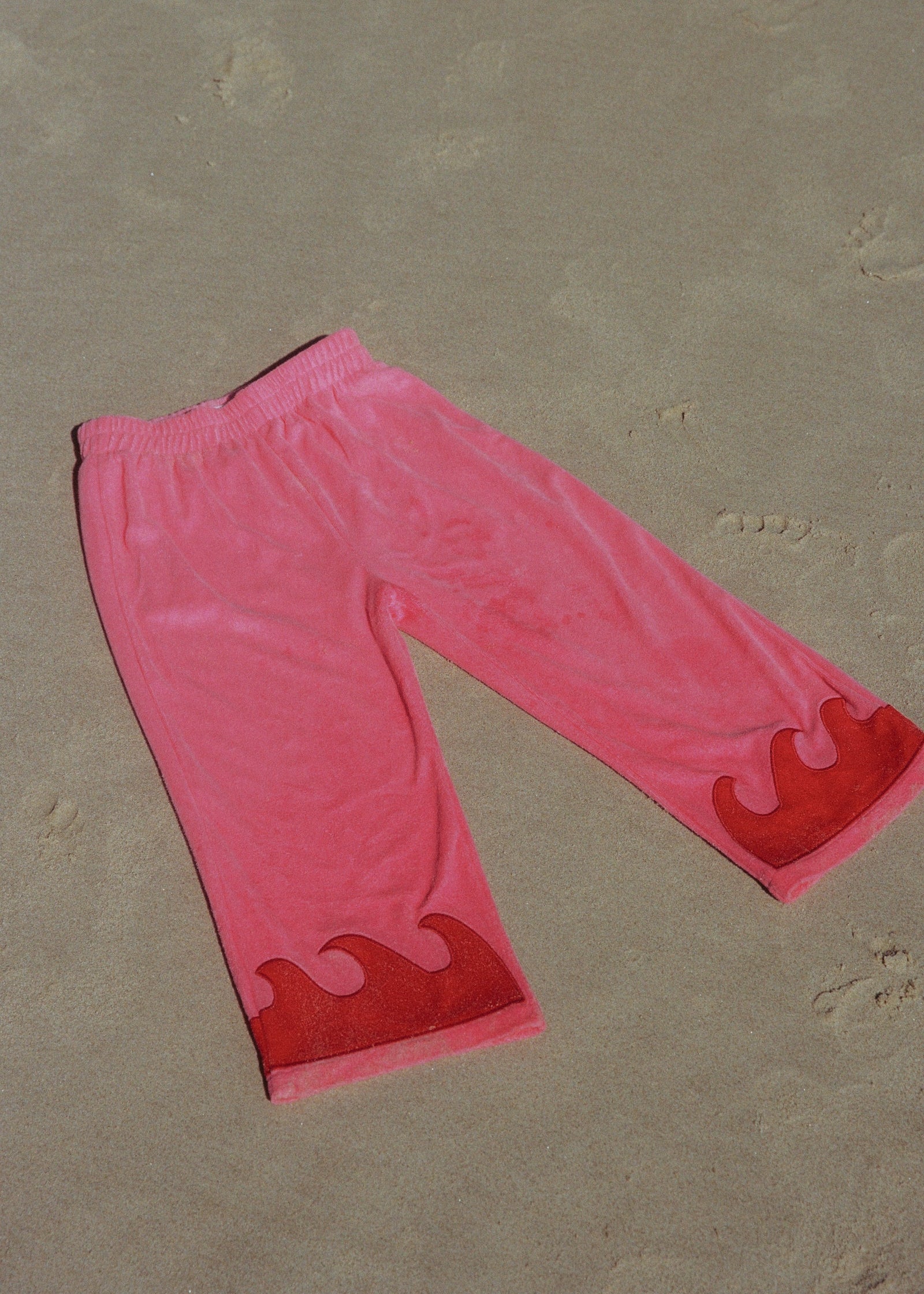 Pink pants with red wave designs on a beige surface
