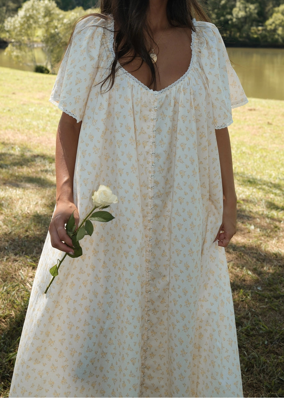 Woman in a white floral dress holding a white rose in a natural setting