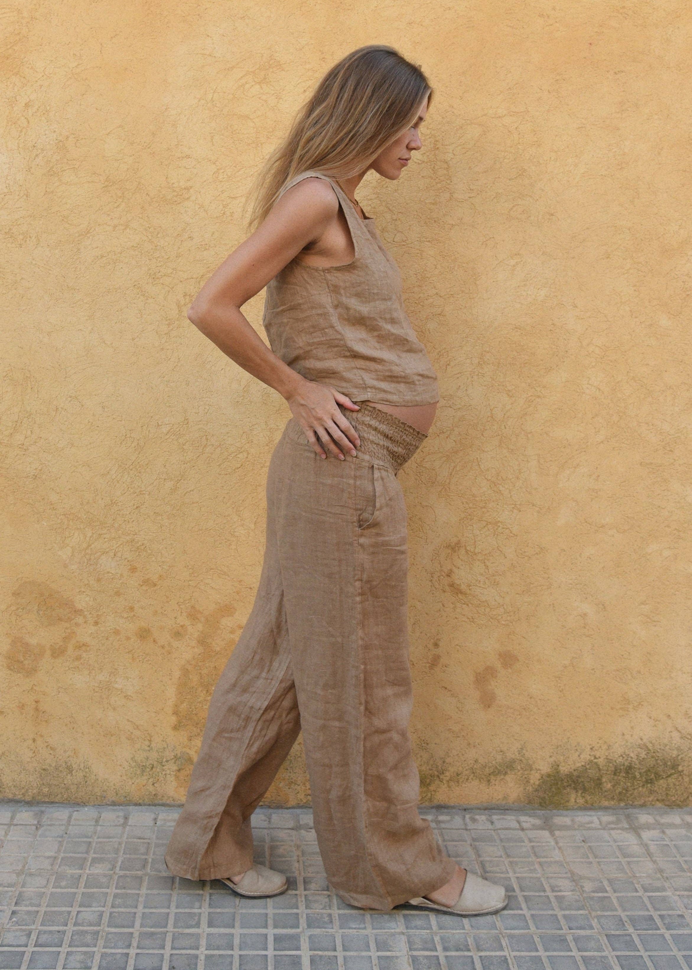 Woman wearing brown linen pants standing against a yellow wall.