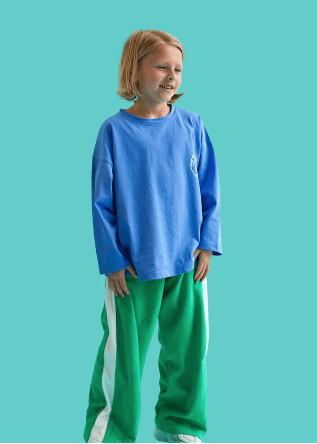 Child wearing a blue long-sleeve shirt and green pants on a teal background