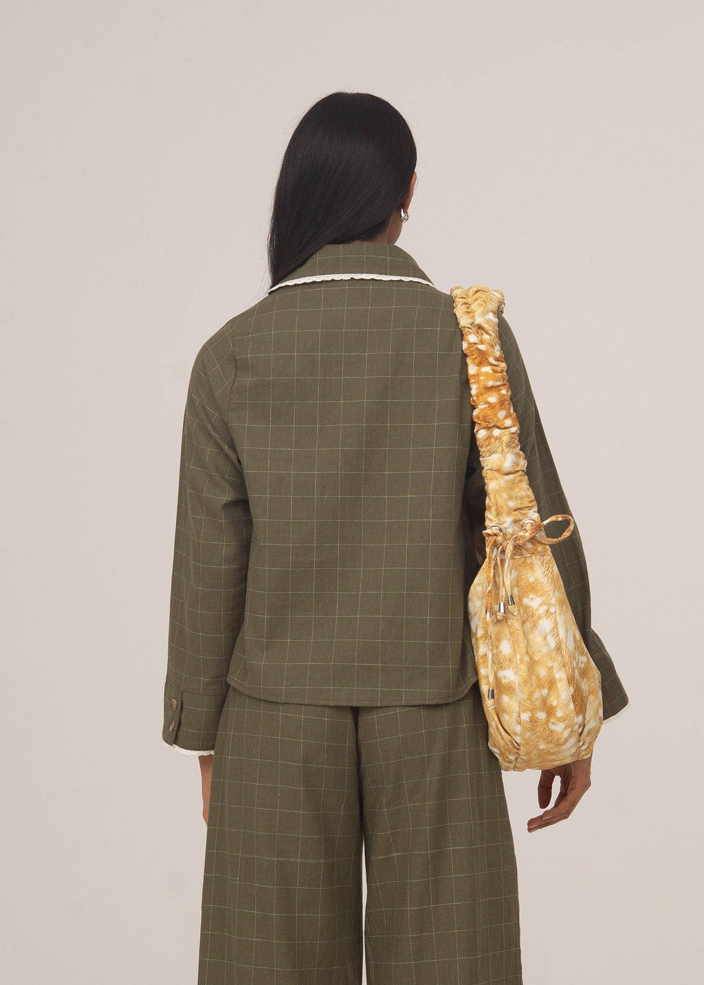 Person wearing a green checkered suit with a yellow textured bag on a plain background