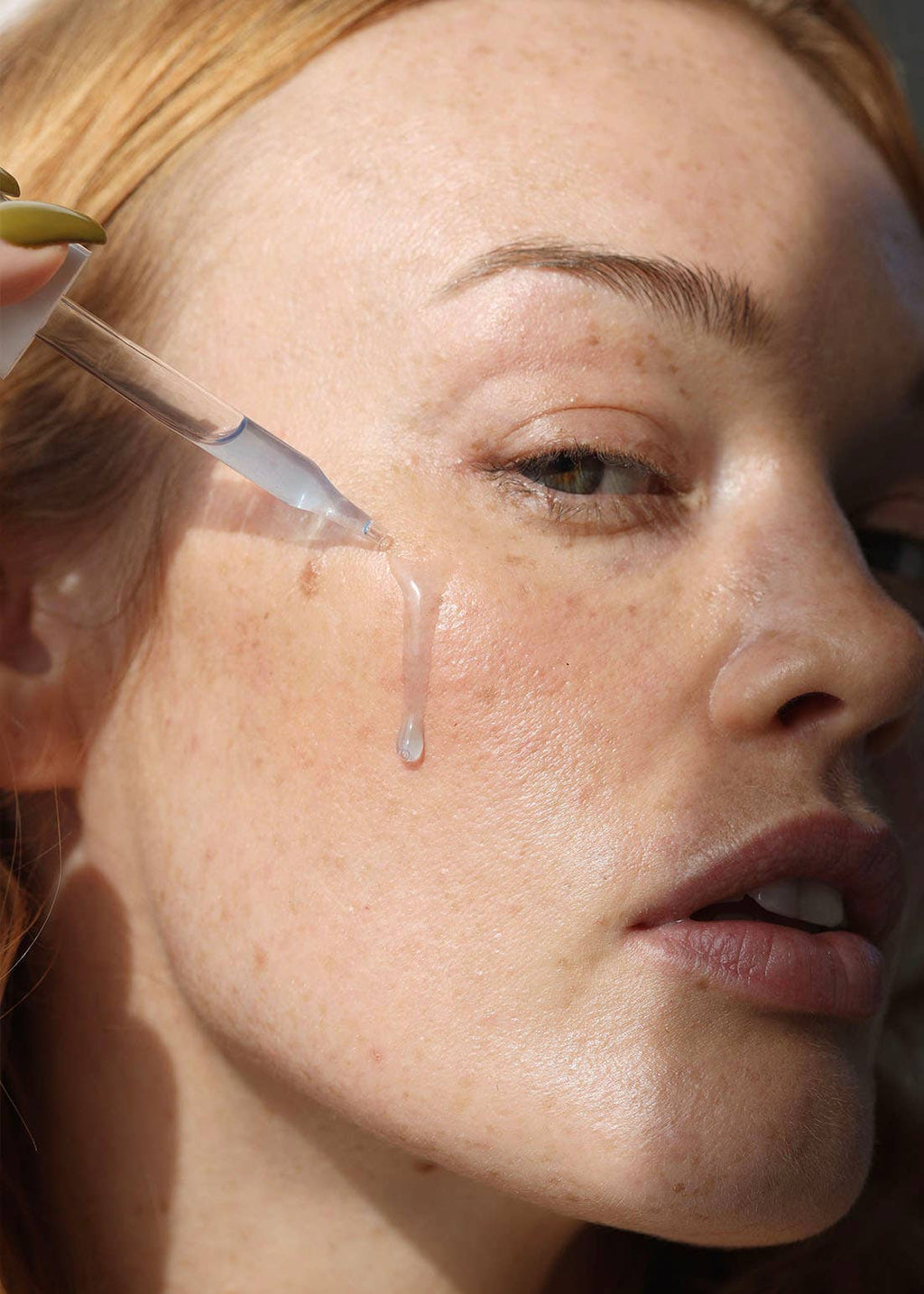 Close-up of a woman's face with a dropper applying liquid to her skin.