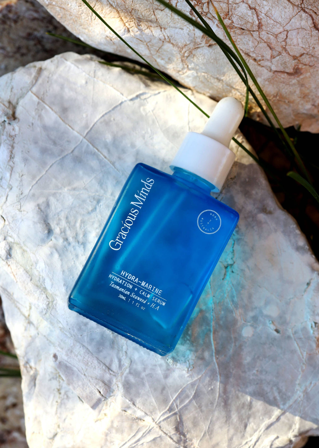 Blue skincare serum bottle with white cap on a stone surface