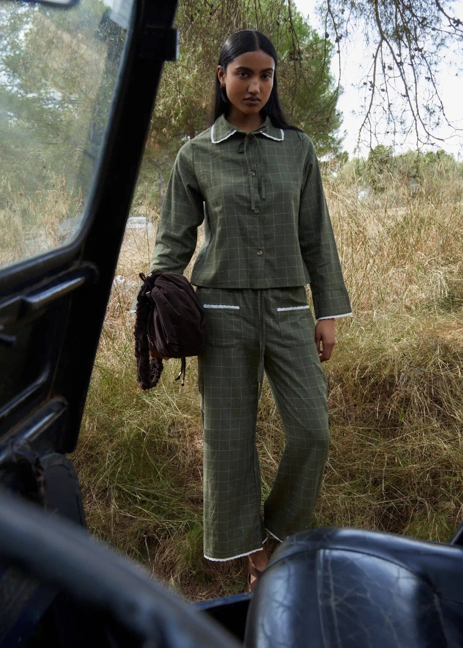 Woman in green outfit standing next to a vehicle in a natural setting