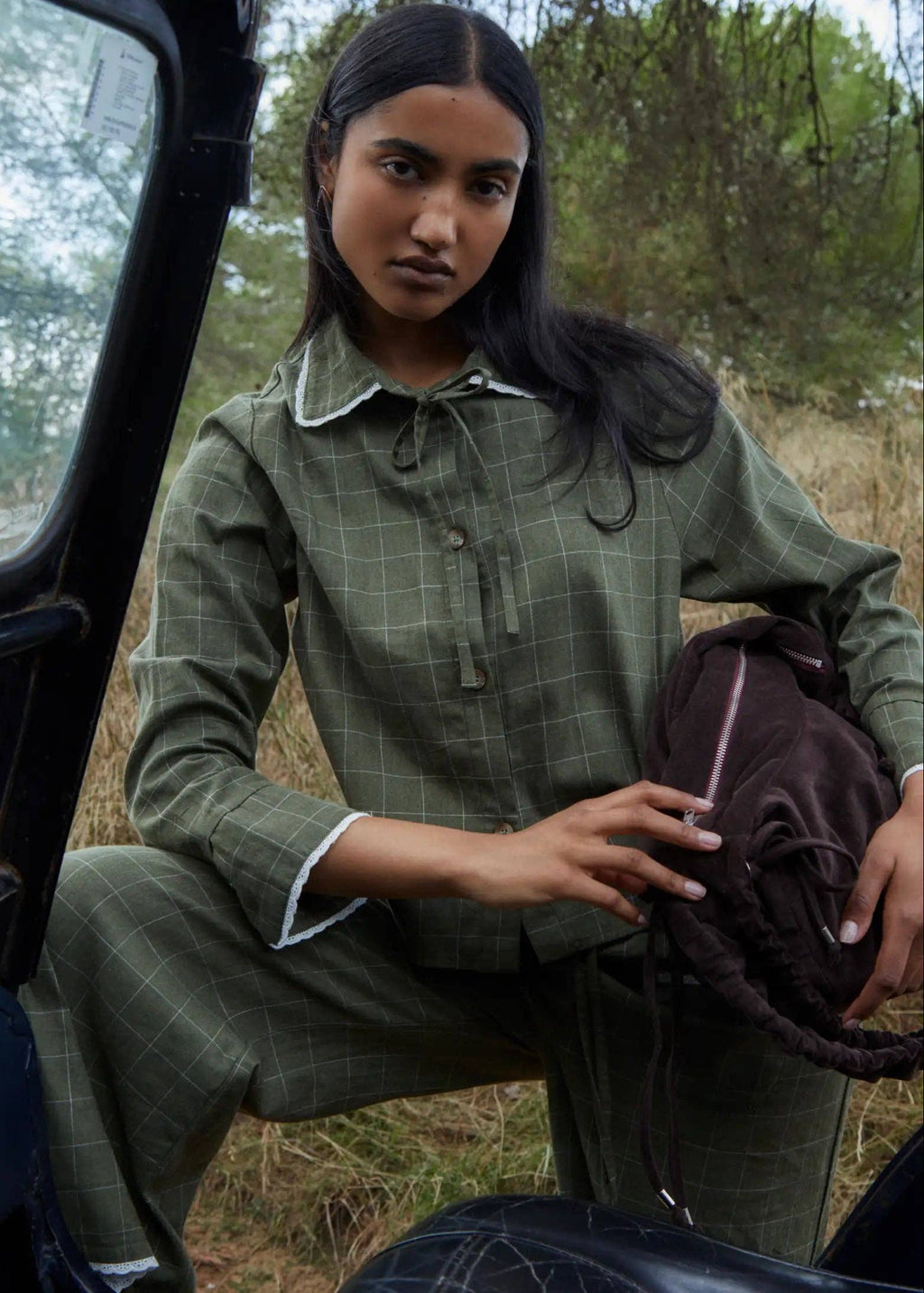 Woman in a green plaid outfit sitting in a vehicle with a forest background