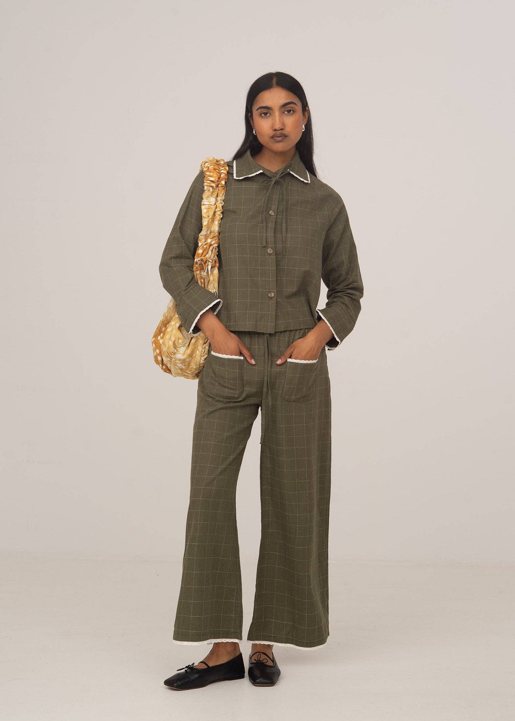 Woman wearing a green plaid outfit with a gold bag on a plain background