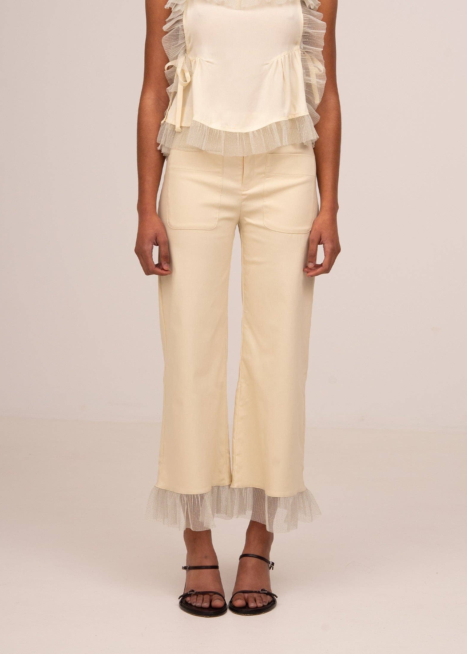 Person wearing a white top and beige pants with tulle details on a plain background