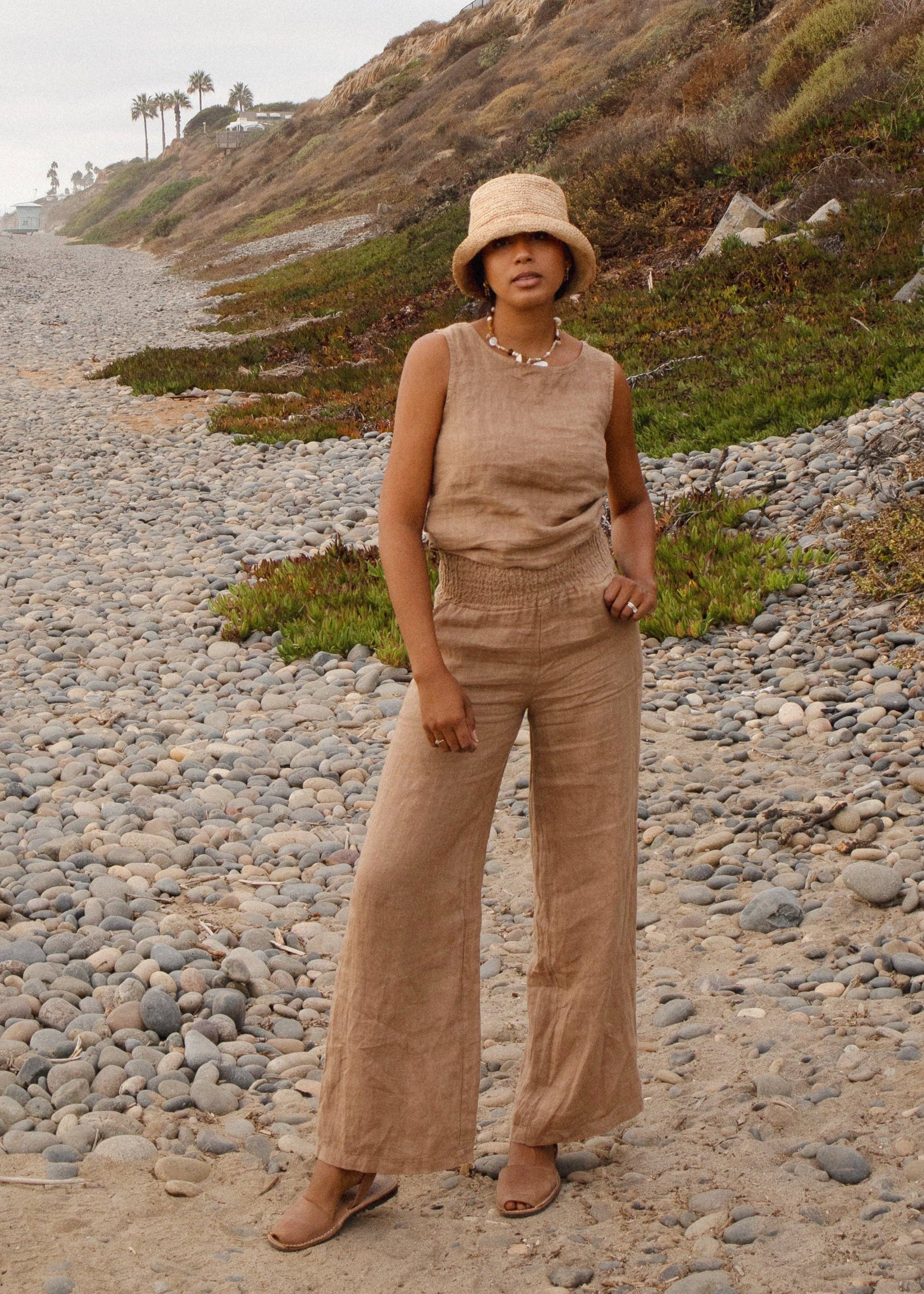 Woman in beige outfit standing on a rocky beach with grassy hillside in the background