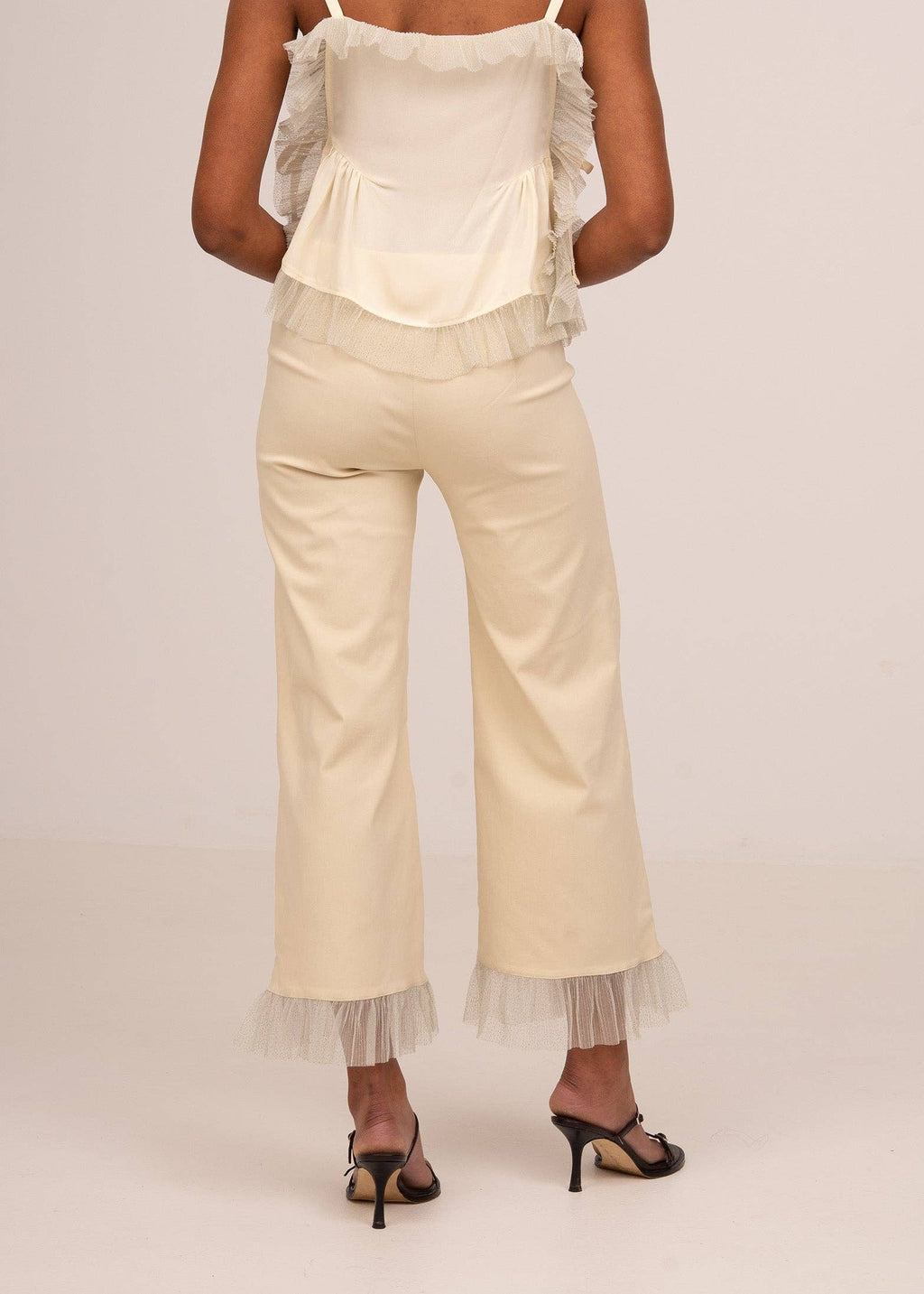 Woman wearing a white top and beige pants with lace details on a plain background