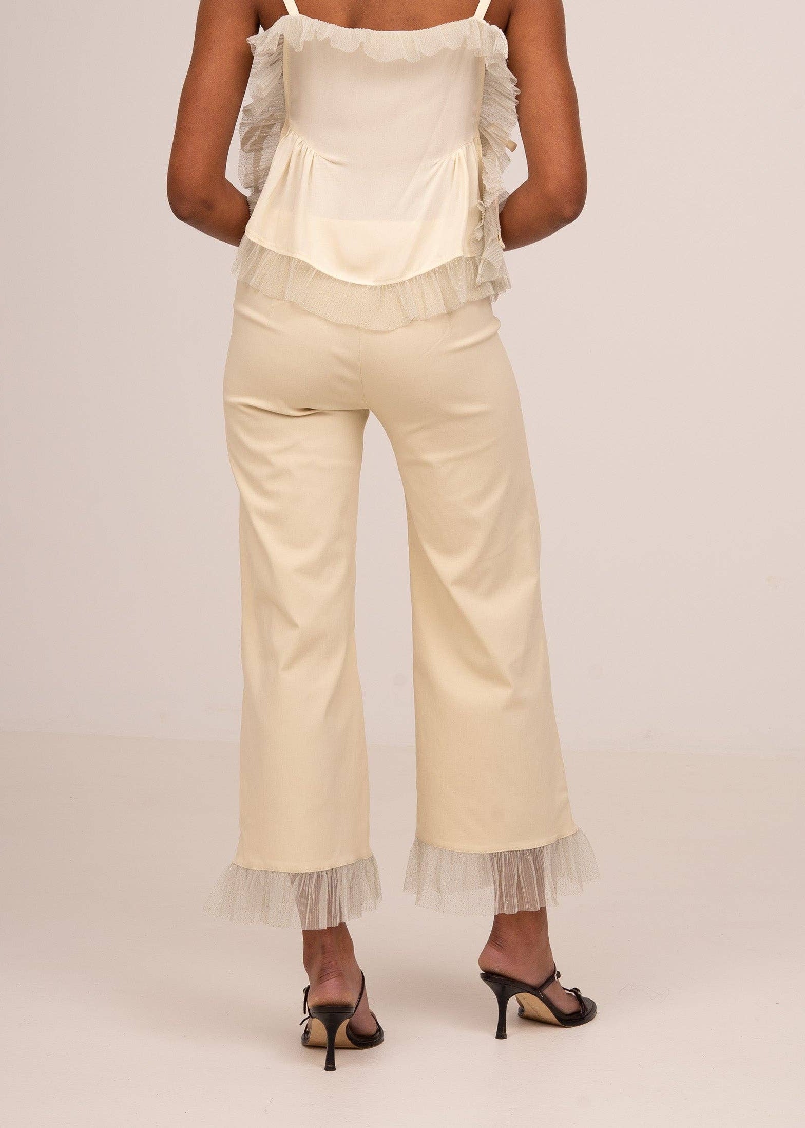 Woman wearing a white top and beige pants with lace details on a plain background