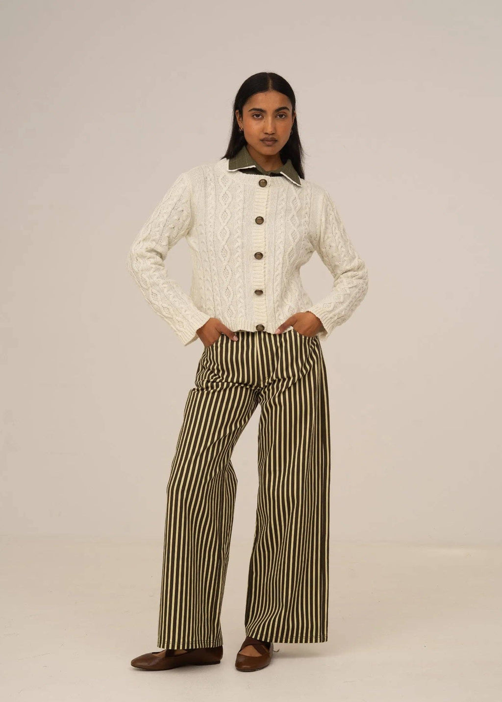 Person wearing a white cable knit sweater and striped pants on a plain background