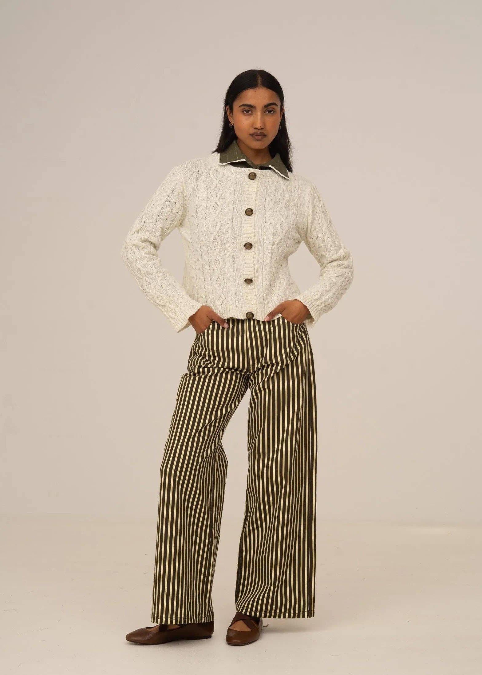 Person wearing a white cable knit sweater and striped pants on a plain background