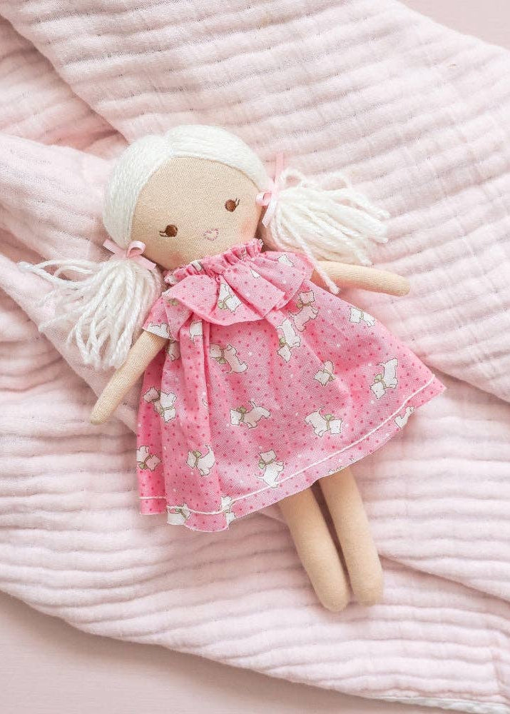 Textile doll with a pink dress on a soft pink fabric background