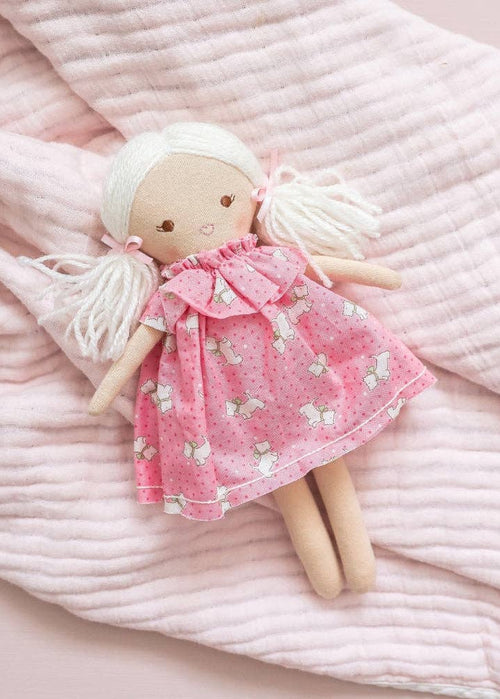 Textile doll with a pink dress on a soft pink fabric background